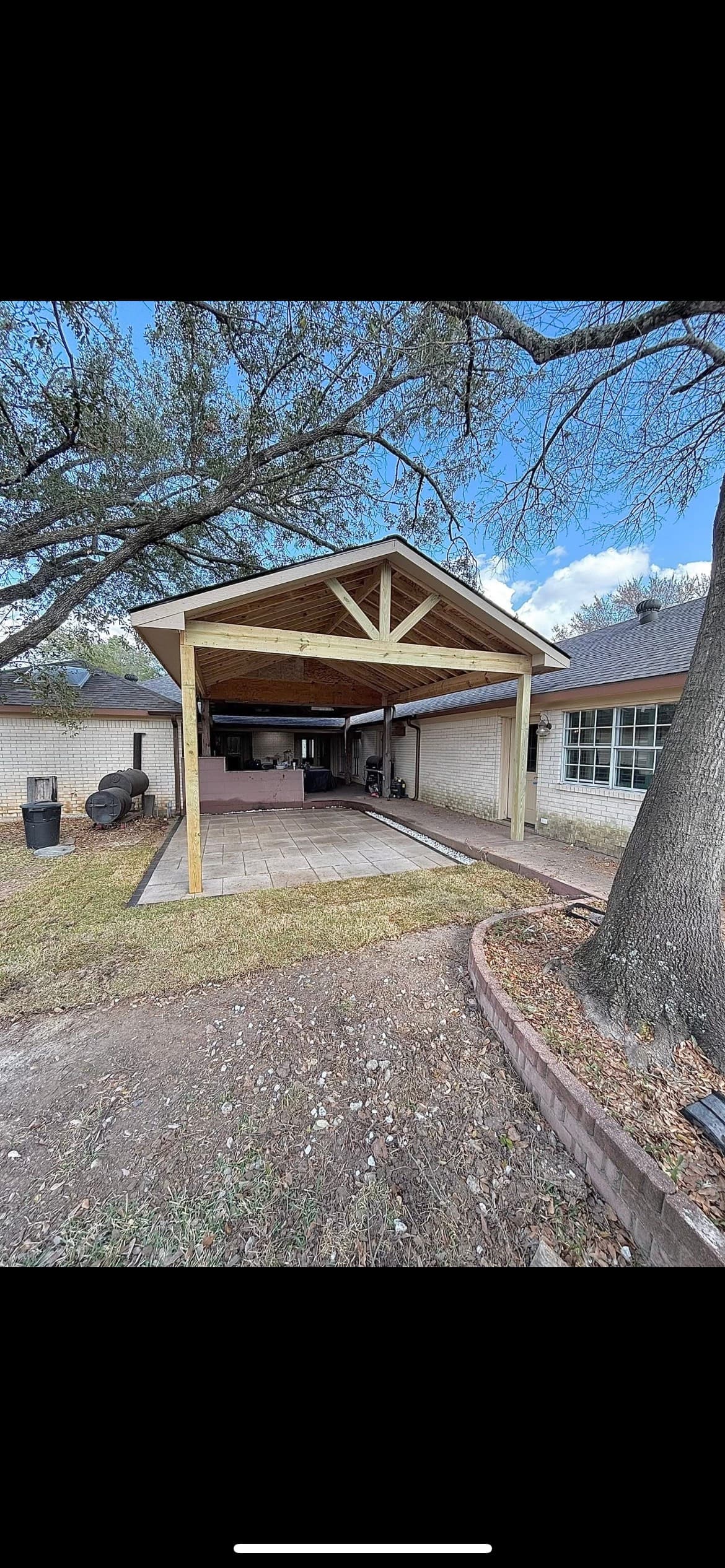 A wooden gabled pavilion covers a stone patio attached to a white brick house.