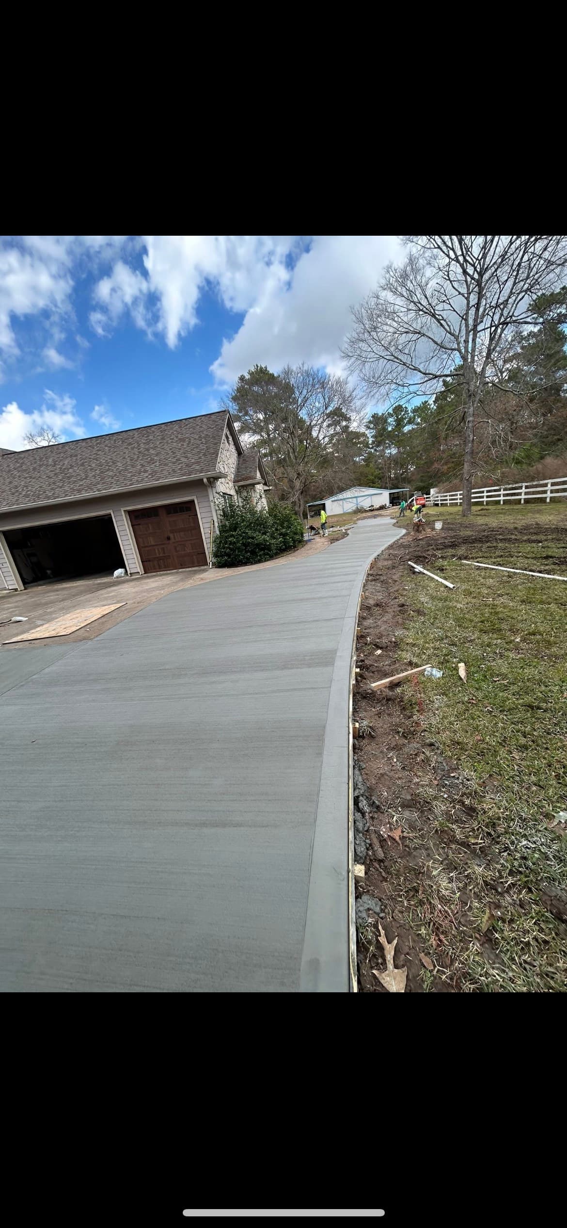 Newly finished curved concrete driveway with a brushed texture leading to a suburban home garage.