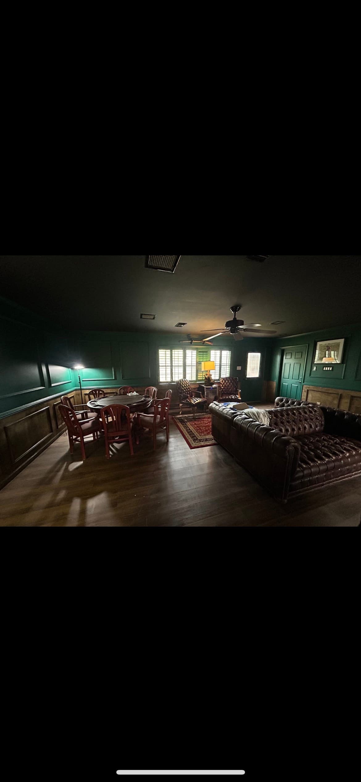 Moody den with dark green walls, a round game table, and a tufted leather sofa.